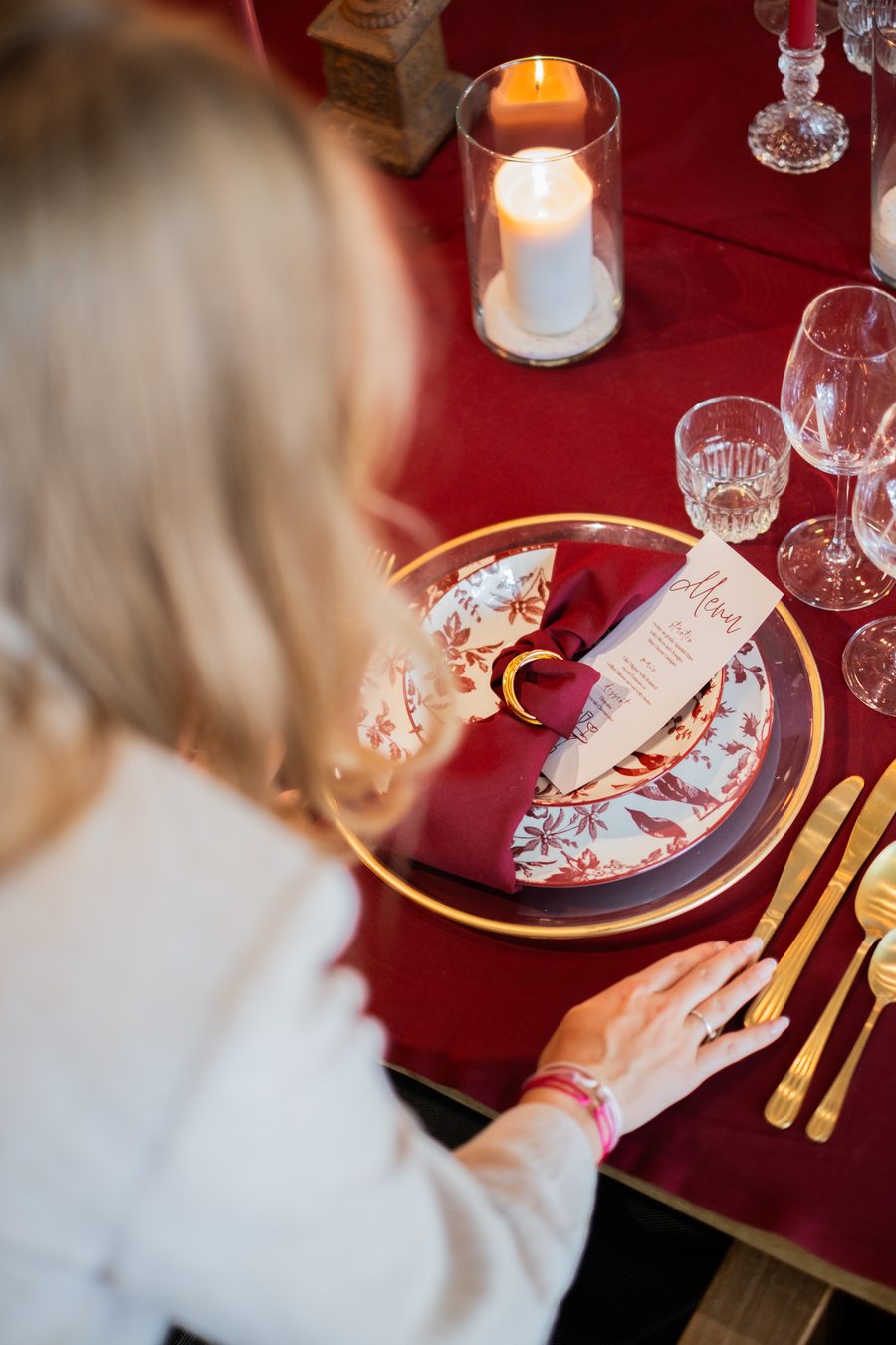 Burgundy tafeldetail met menukaart, kaarslicht en gouden bestek