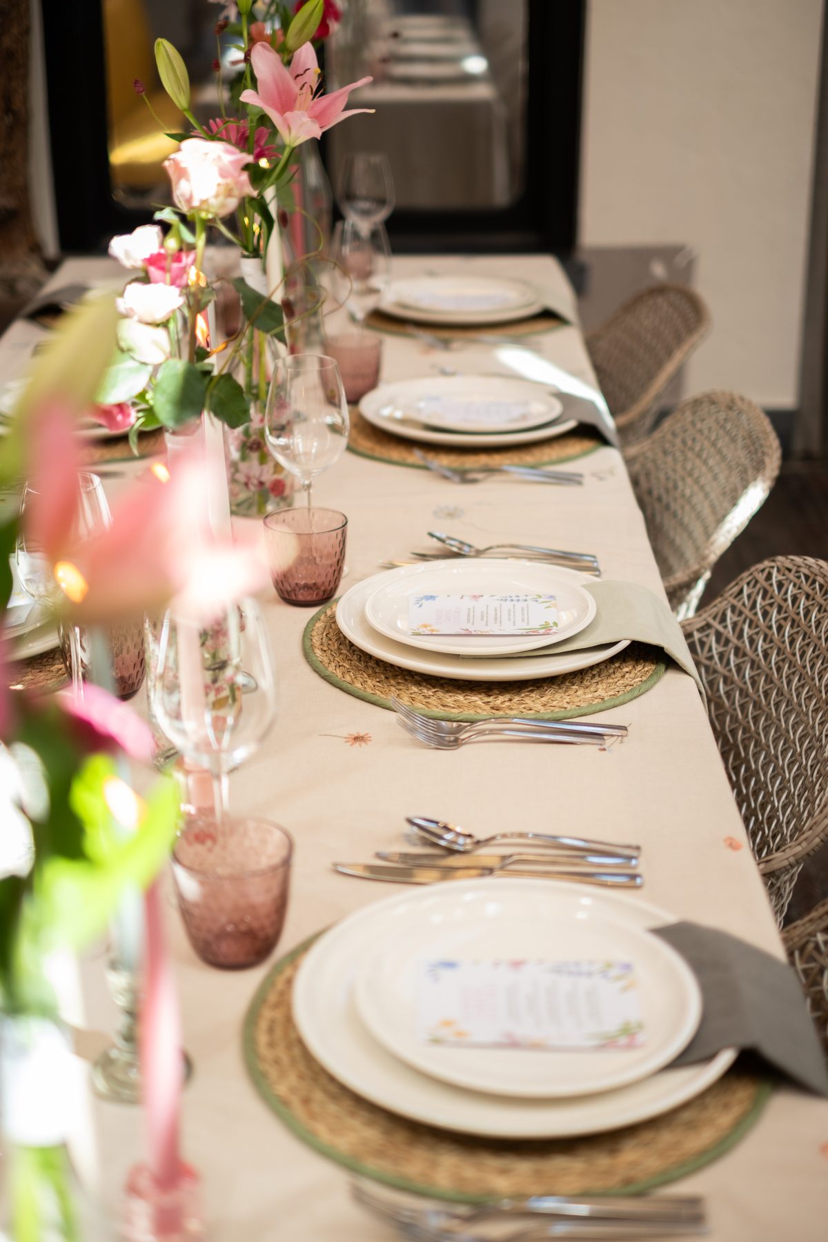 Gedekte tafel met roze bloemen, servies en rotan stoelen